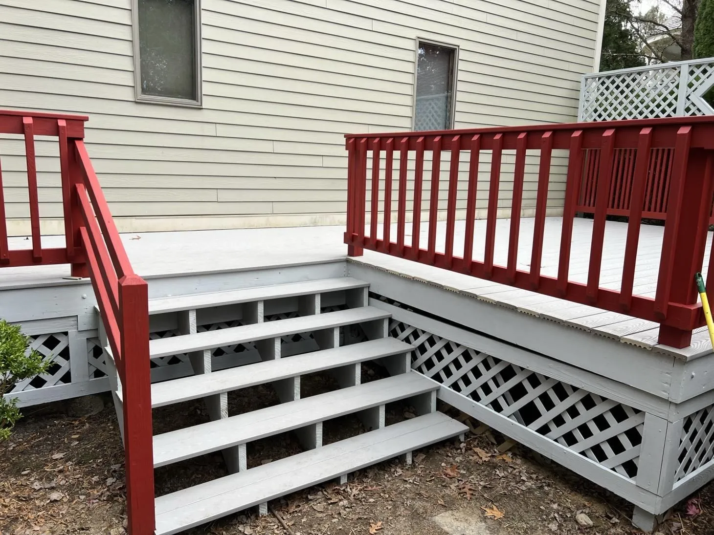 Deck stairs with gray treads, red railings and lattice skirting