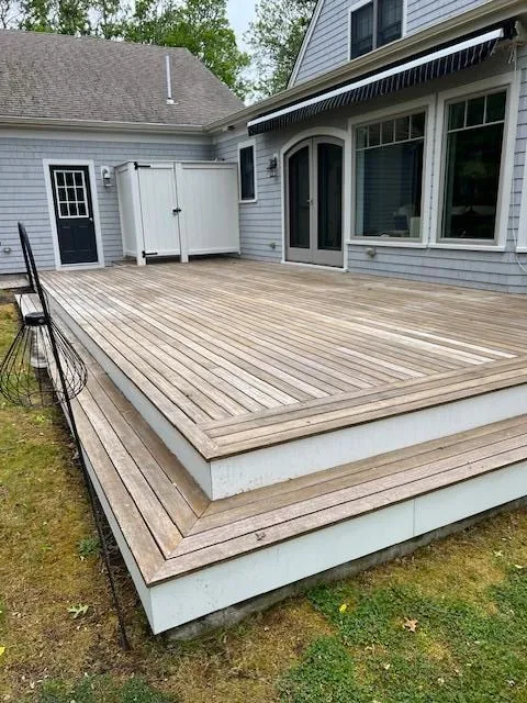 Wide wood deck with wraparound steps behind a gray shingled house