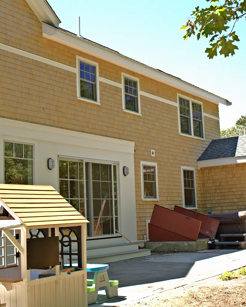 Back of a new cedar shingle house with white trim and sliding doors